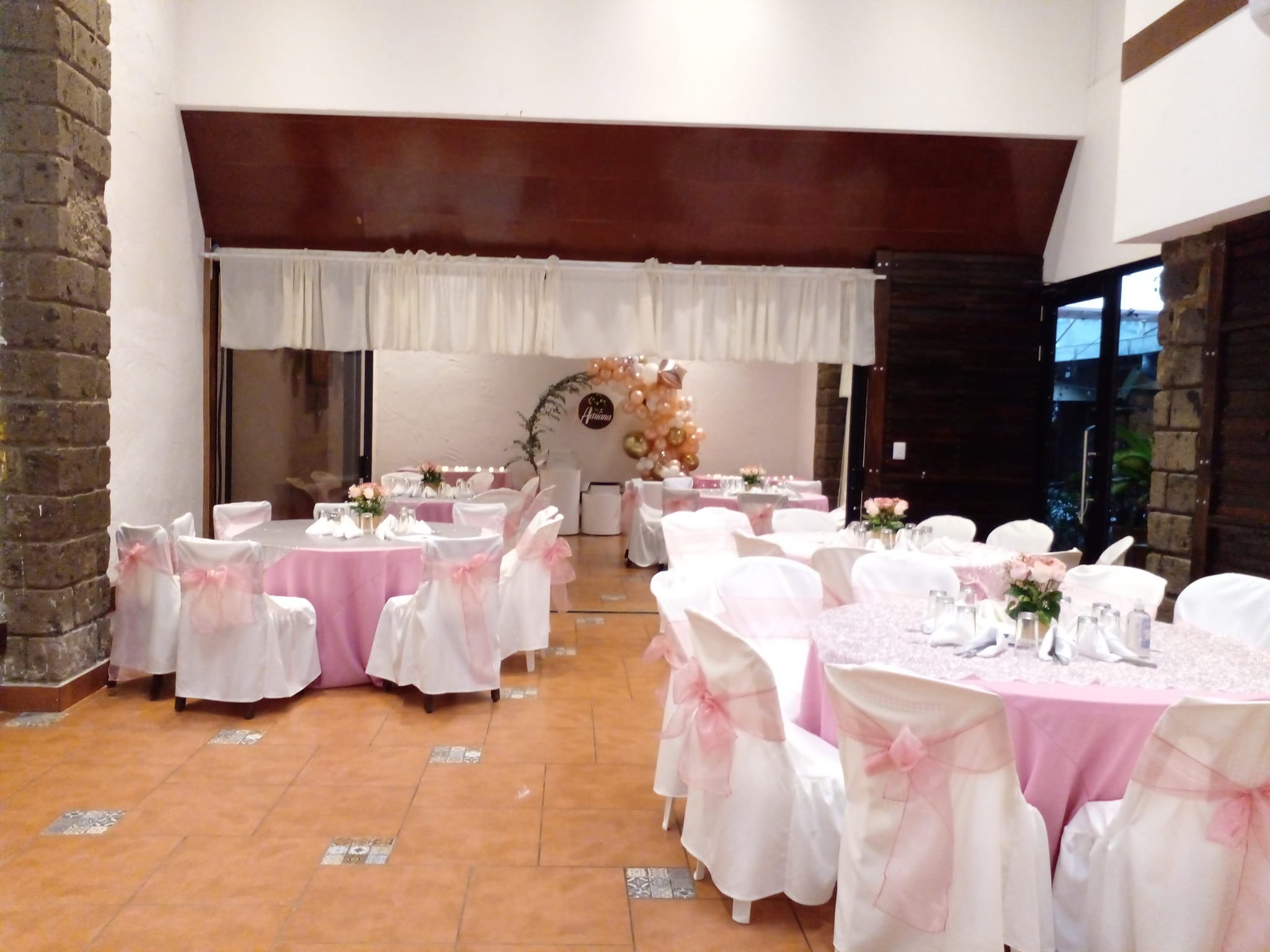 Salón decorado con arco de globos dorados y rosados para una celebración